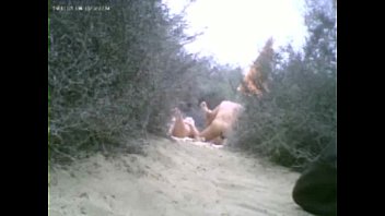 Porn; woman giving blowjob to several men in sand dunes